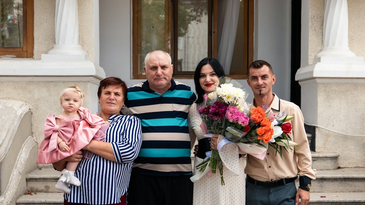 A family on stone steps, two adults holding a baby and a flower bouquet